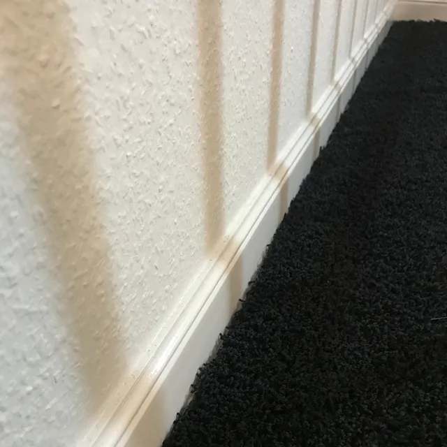 Dunkler Teppich, weiße Wand und Fußleiste