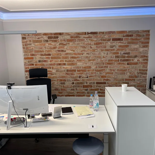 Büro mit Tisch, Lichtleisten und Mauerwand